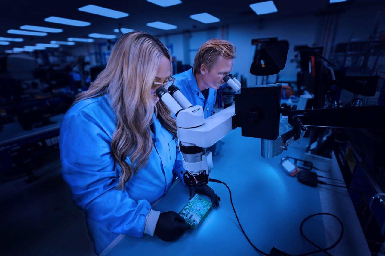 female and male techicians looking through microscopes at circuit boards